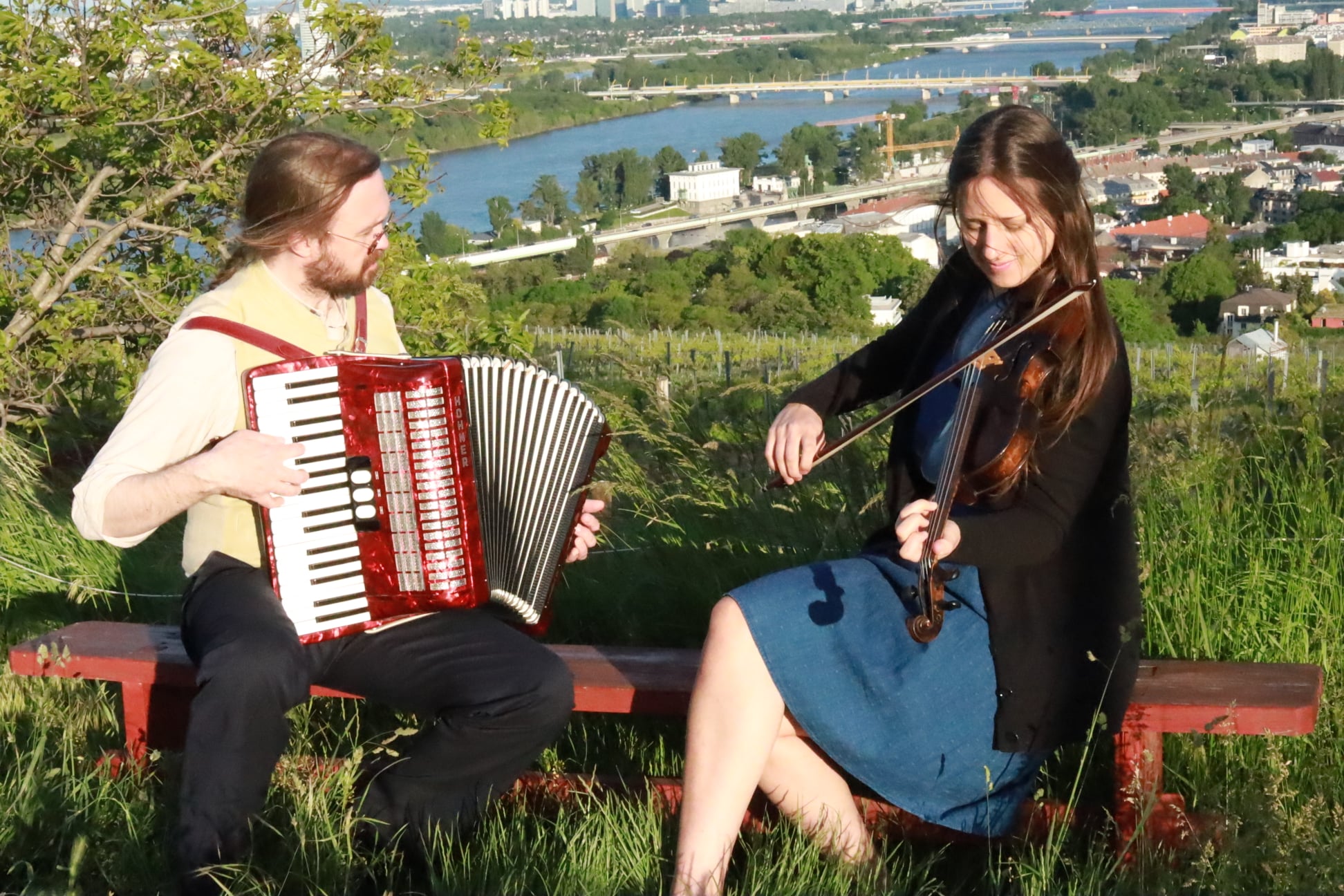 Anna Breger and Johannes G. Schwarz of Wiener Miniorchester — violin and accordion, on a bench overlooking the Danube